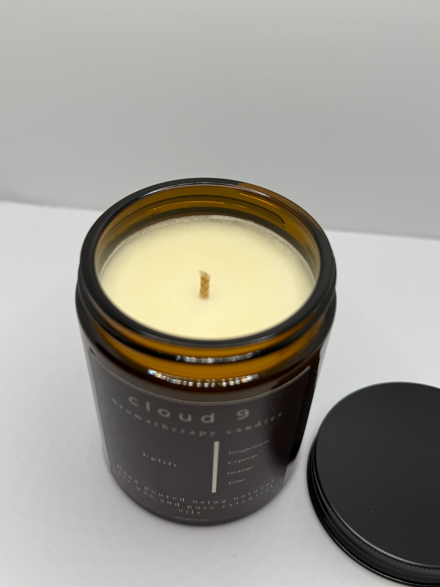 Lit ‘Uplift’ soy candle glowing in bright natural light; the flame contributes to a refreshing, mood-lifting citrus ambiance.