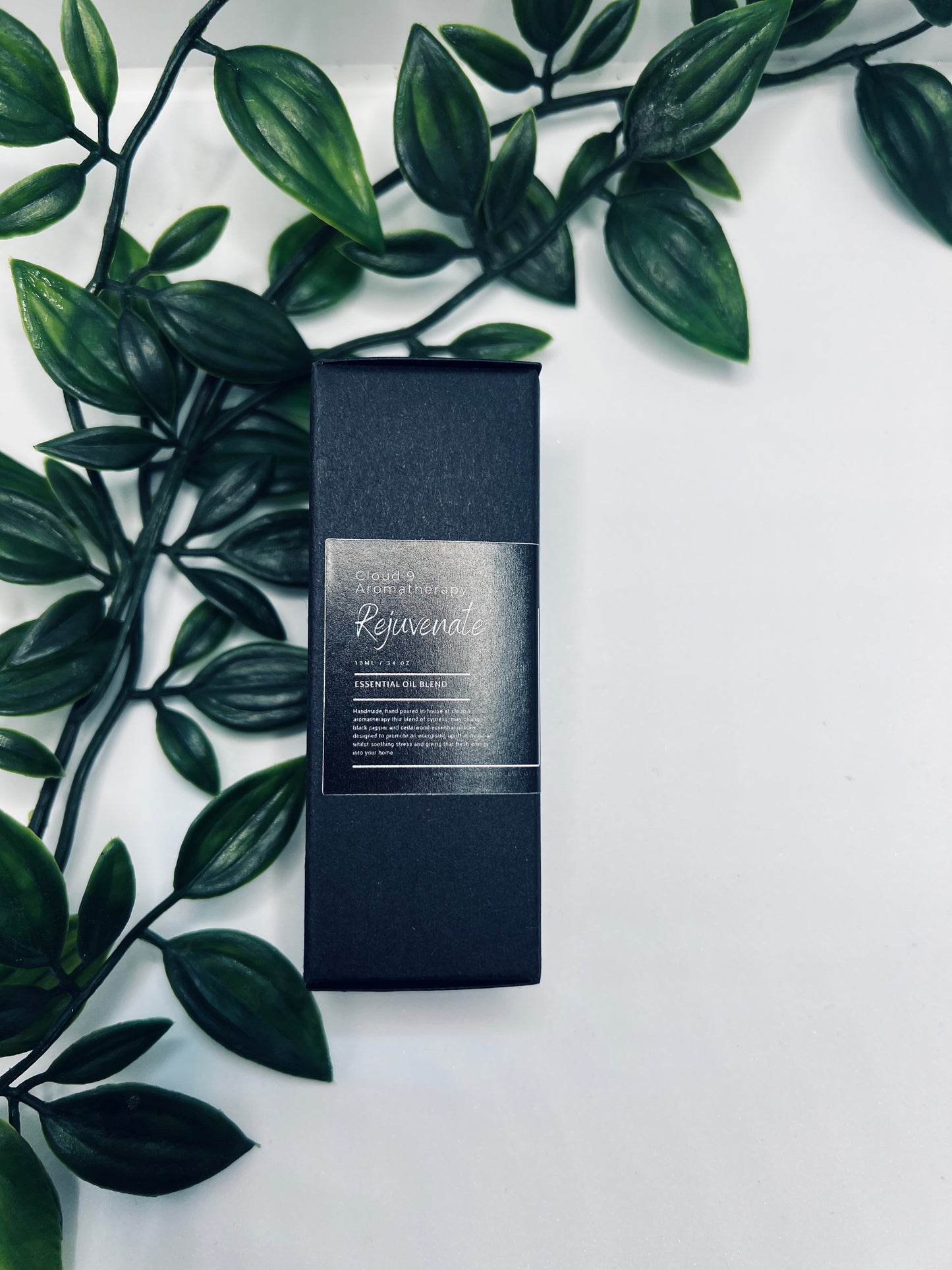 Close-up of ‘Rejuvenate’ essential oil in a dropper-style bottle with foliage backdrop, highlighting its premium hand-poured presentation.