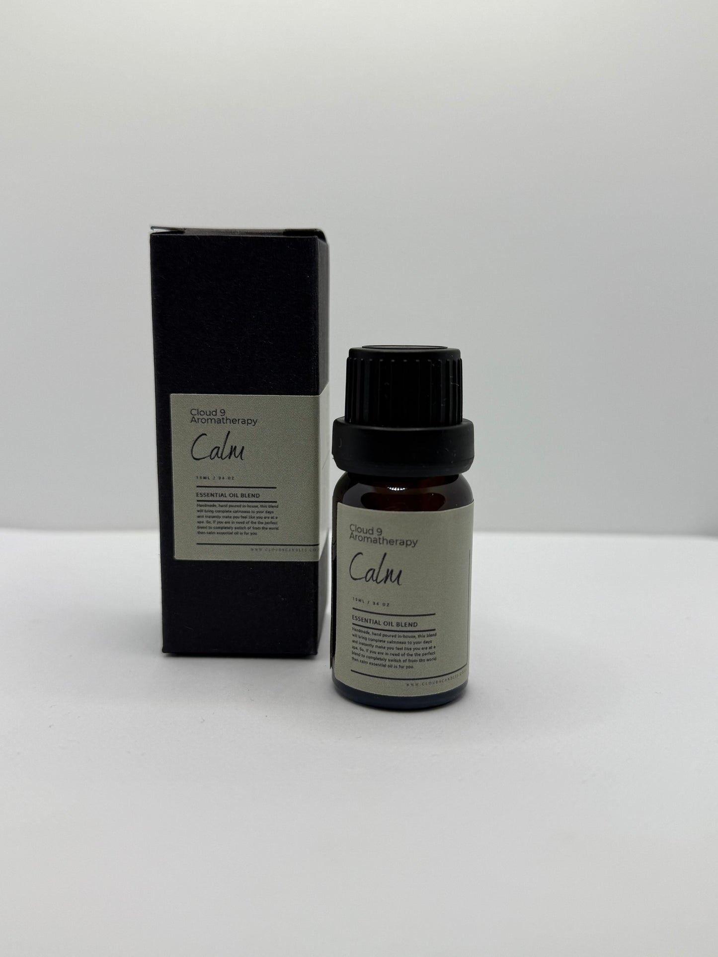 Close-up of a hand-poured ‘Calm’ essential oil blend bottle beside fresh ylang ylang and marjoram blooms, suggesting a soothing aromatherapy ritual.