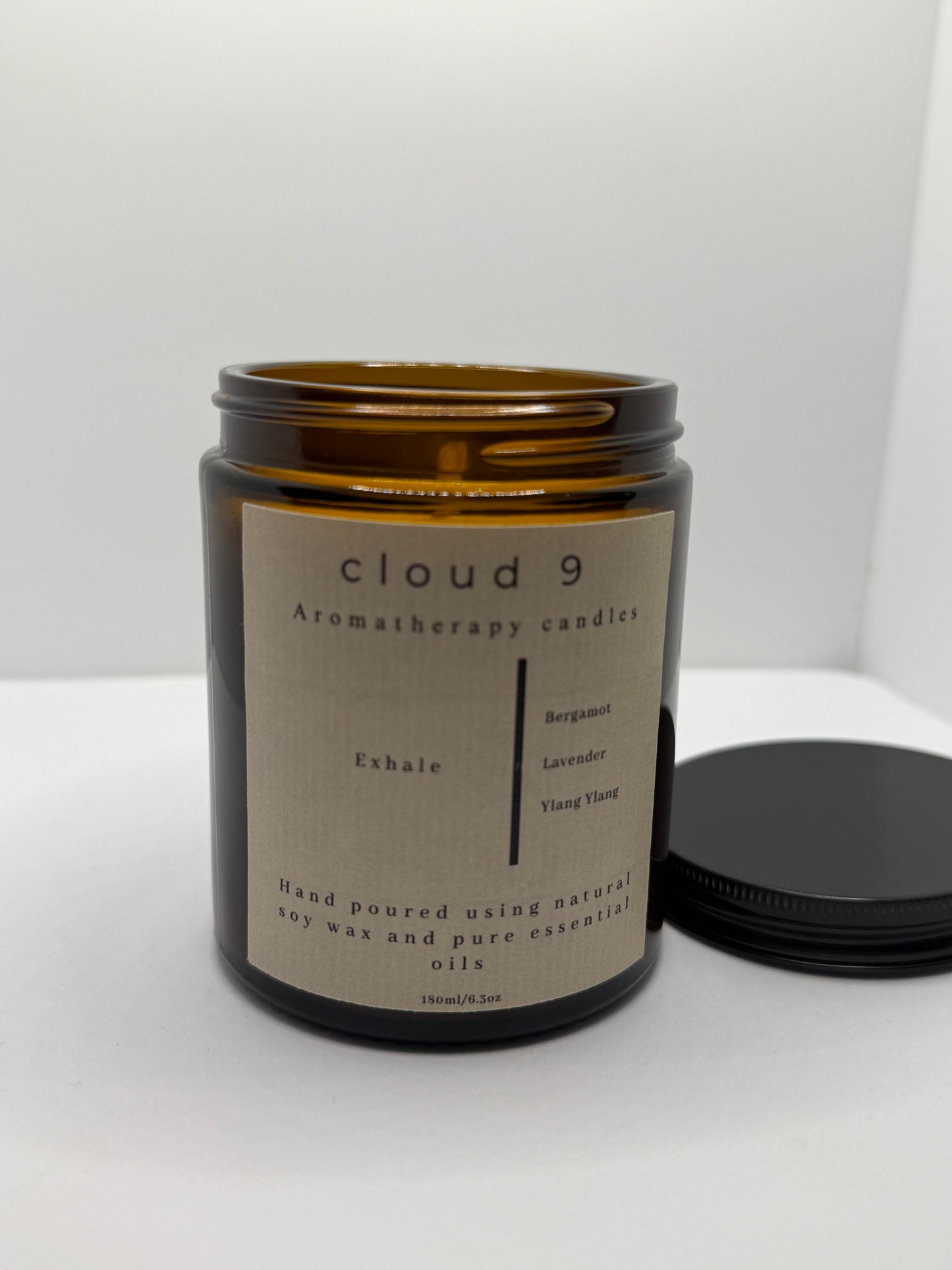 Amber glass jar candle labeled ‘Exhale’ containing an aromatherapy soy wax blend of bergamot, lavender, and ylang ylang, standing upright against a clean, neutral background.