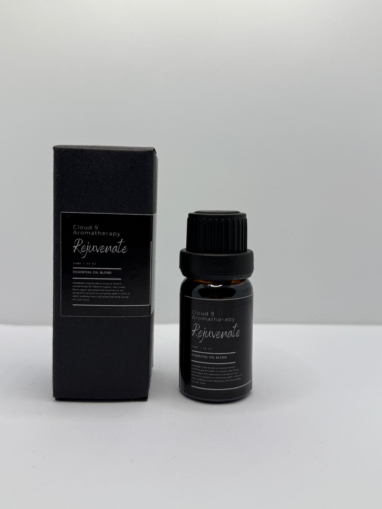 Hand-poured ‘Rejuvenate’ 10 ml essential oil bottle in amber glass, styled with natural greenery to reflect its energizing blend of cypress, may chang, black pepper, and cedarwood