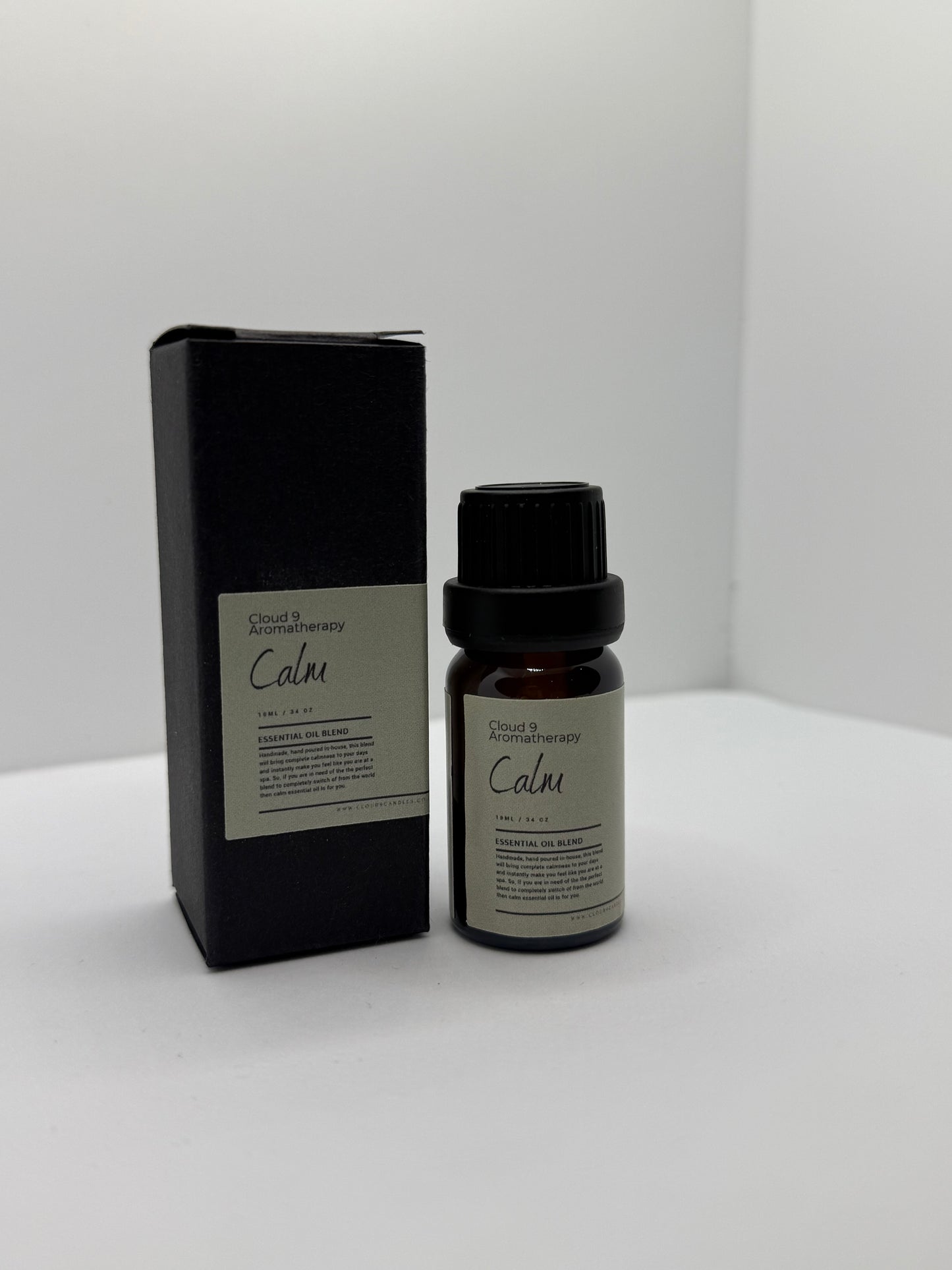 Close-up of a hand-poured ‘Calm’ essential oil blend bottle beside fresh ylang ylang and marjoram blooms, suggesting a soothing aromatherapy ritual.
