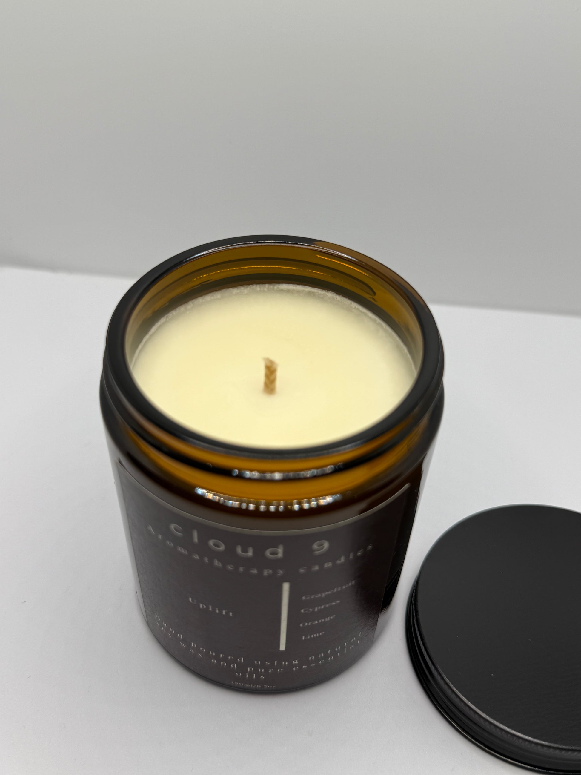 Lit ‘Uplift’ soy candle glowing in bright natural light; the flame contributes to a refreshing, mood-lifting citrus ambiance.