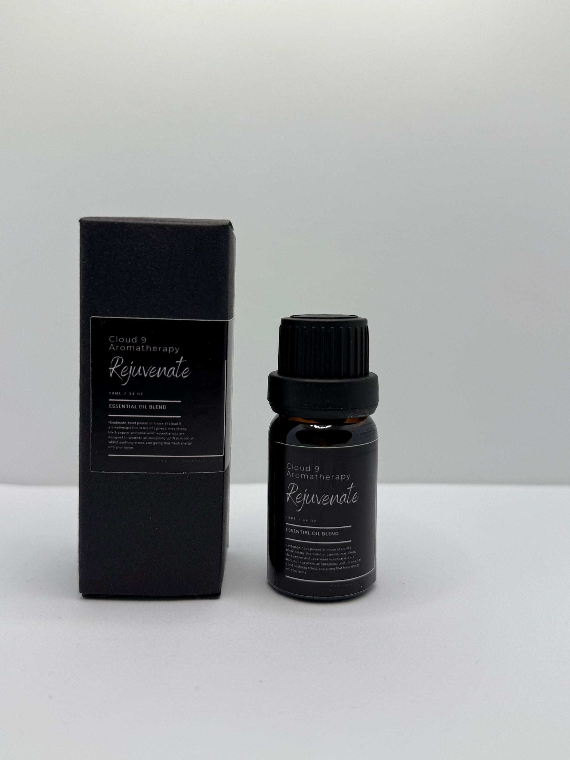 Hand-poured ‘Rejuvenate’ 10 ml essential oil bottle in amber glass, styled with natural greenery to reflect its energizing blend of cypress, may chang, black pepper, and cedarwood