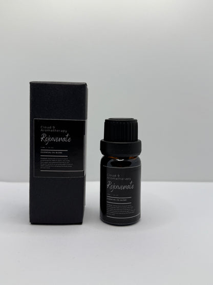 Hand-poured ‘Rejuvenate’ 10 ml essential oil bottle in amber glass, styled with natural greenery to reflect its energizing blend of cypress, may chang, black pepper, and cedarwood