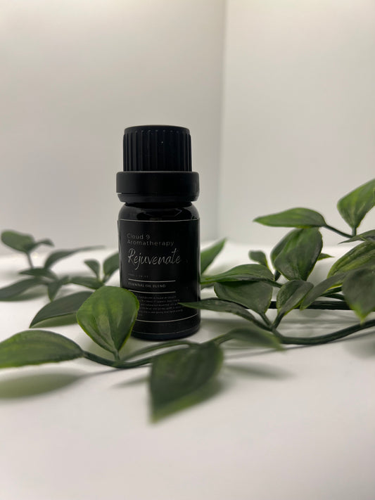 Amber glass bottle of ‘Rejuvenate’ essential oil blend surrounded by greenery, showcasing natural aromatherapy packaging.