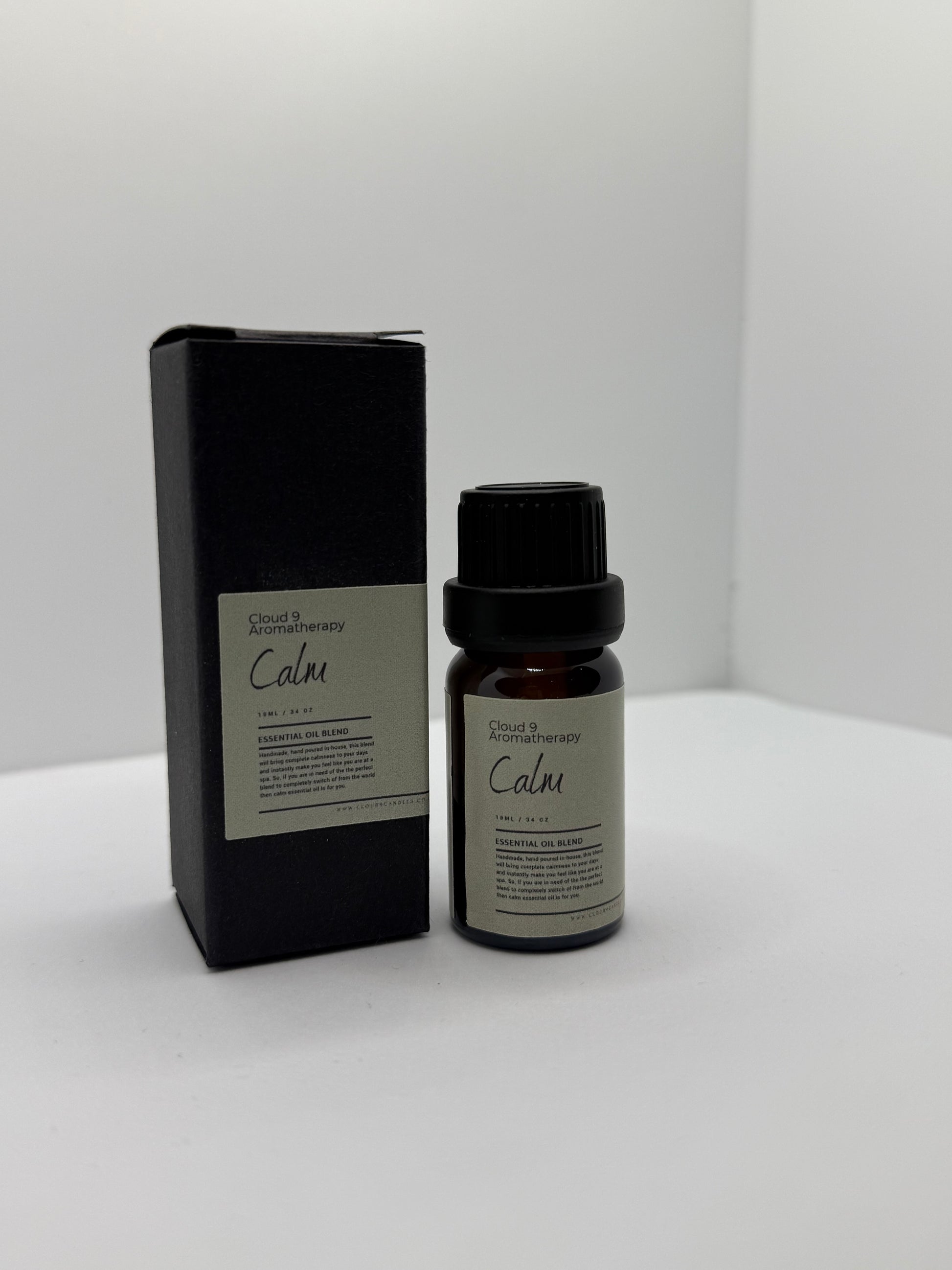 Close-up of a hand-poured ‘Calm’ essential oil blend bottle beside fresh ylang ylang and marjoram blooms, suggesting a soothing aromatherapy ritual.