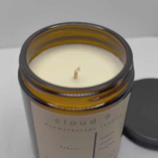 Amber ‘Exhale’ aromatherapy candle with decorative green foliage beside it, highlighting the candle’s calming scent profile of lavender and bergamot.
