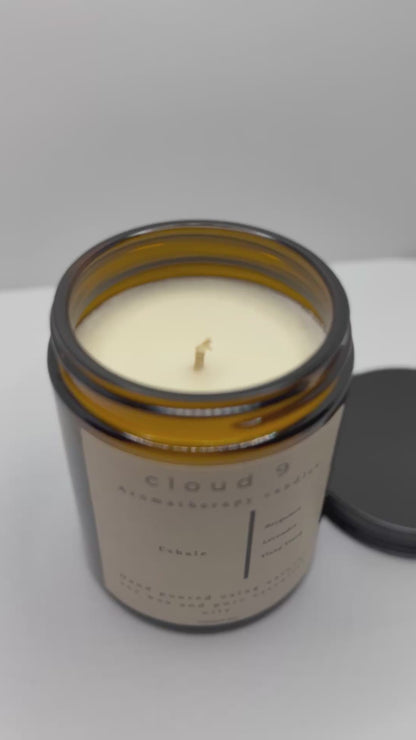 Amber ‘Exhale’ aromatherapy candle with decorative green foliage beside it, highlighting the candle’s calming scent profile of lavender and bergamot.